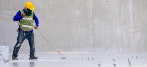 Person in protective gear using a floor polisher on a concrete floor.